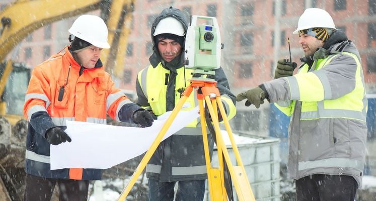 bouwvakkers proberen te werken met een tekening in de hand en een laser. Het sneeuwt en ze kijken moeilijk.