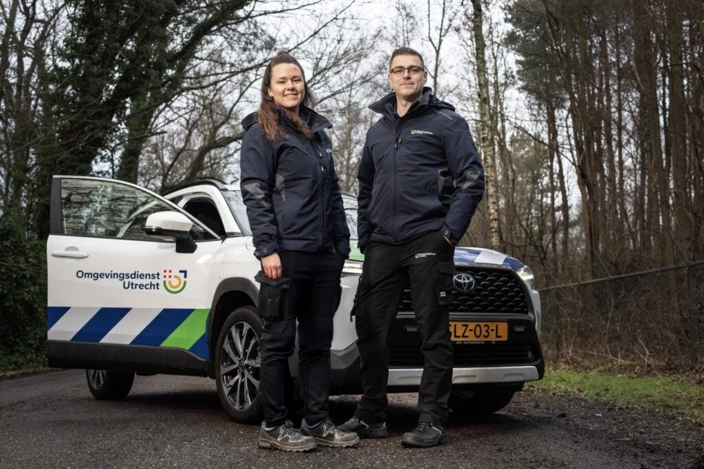 ODU medewerkers staan in bosrijke omgeving voor hun auto en kijken trots de camera in
